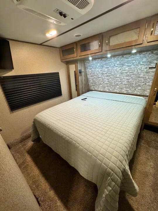 Experience comfort in this RV rental bedroom: features a cozy bed, textured wall, overhead storage, and AC for a great stay.. Keystone RV Sprinter Campfire Edition 2020