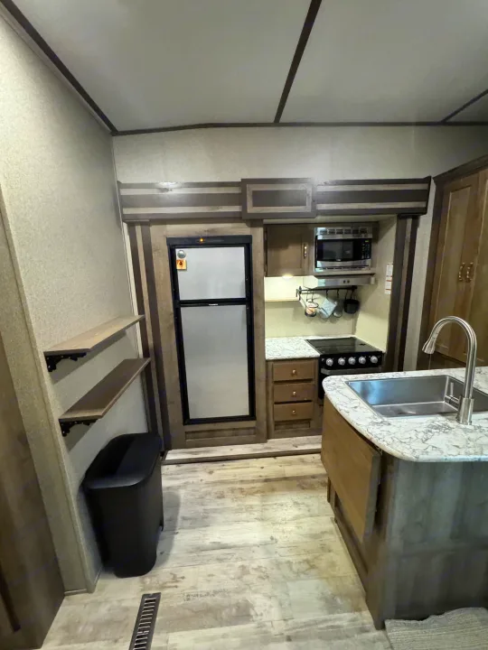 Modern RV rental kitchen with fridge, microwave, stove, sink, and ample storage, ready for your road trip adventures.. Keystone RV Sprinter Campfire Edition 2020