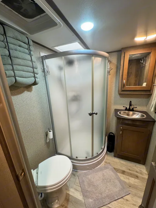 Compact RV rental bathroom with a rounded shower, toilet, sink vanity, and textured window shades. Practical and well-lit.. Keystone RV Sprinter Campfire Edition 2020