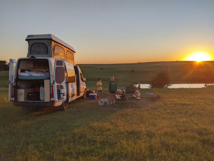 RV rental adventure! Family enjoys a scenic sunset campout with their pop-top camper van by a pond.. Mercedes-Benz Sprinter 2020