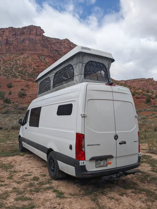 White Sprinter pop-top camper van for an RV rental, parked in a desert with red rock mountains.. Mercedes-Benz Sprinter 2020