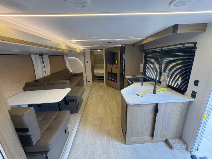 Bright RV rental interior featuring a modern living area with couch & table, full kitchen, and bedroom access.. Forest River Salem Cruise Lite 26ICE 2025