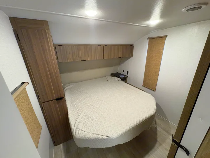 Well-lit RV rental bedroom with a large bed, light-colored bedding, overhead storage cabinets, and a tall wardrobe.. Forest River Salem Cruise Lite 26ICE 2025
