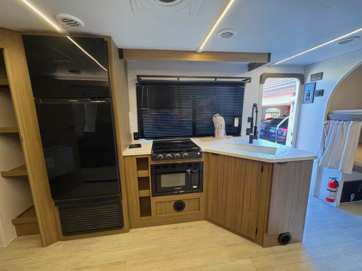 An RV rental kitchen view: fridge, stove, sink, microwave. Modern interior with wood accents & strip lighting.. Forest River Salem Cruise Lite 26ICE 2025
