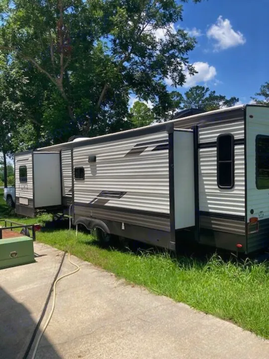 Large RV rental with extended slide-outs, parked on grass next to a driveway under a blue sky and green trees.. Forest River Puma 2023