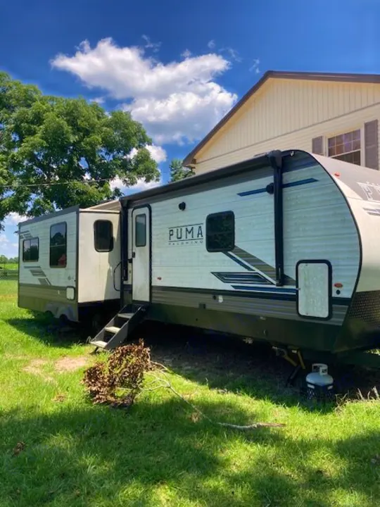 PUMA Palomino RV rental parked on grass, featuring an extended slide-out & awning, under a blue sky. Perfect for travel!. Forest River Puma 2023