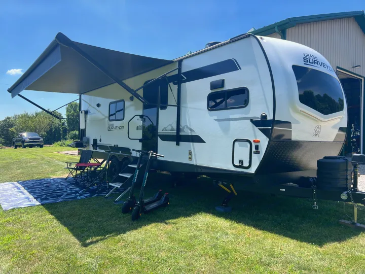 Spacious Grand Surveyor travel trailer for rv rental, featuring an awning, outdoor chairs, and scooters in a sunny campsite setting.. Forest River Grand Surveyor 2024