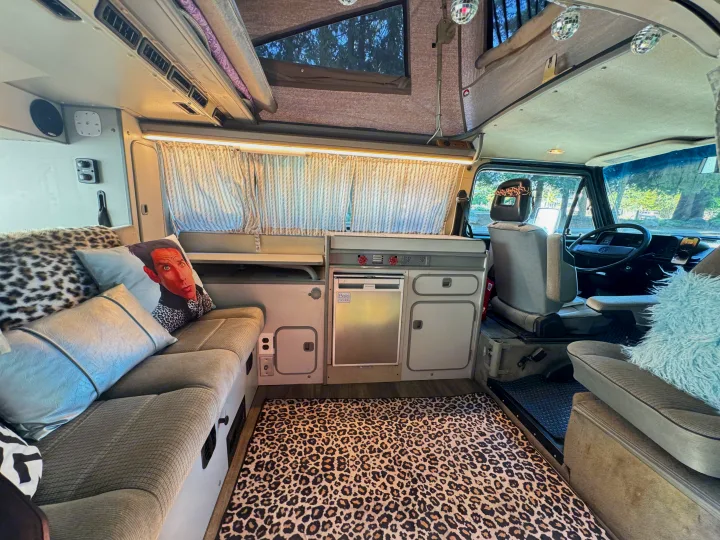 Explore this fun RV rental interior, featuring a leopard print rug, sofa bed, compact kitchenette, and a pop-top roof.. Volkswagen T3 Westfalia 1987