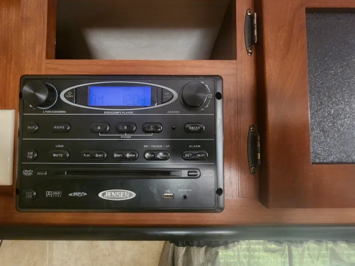 A close-up of a Jensen AWM965 RV entertainment system, displaying AM 12:03, found in an RV rental unit.. Aspen Trail Aspen Trail Trailer 2013