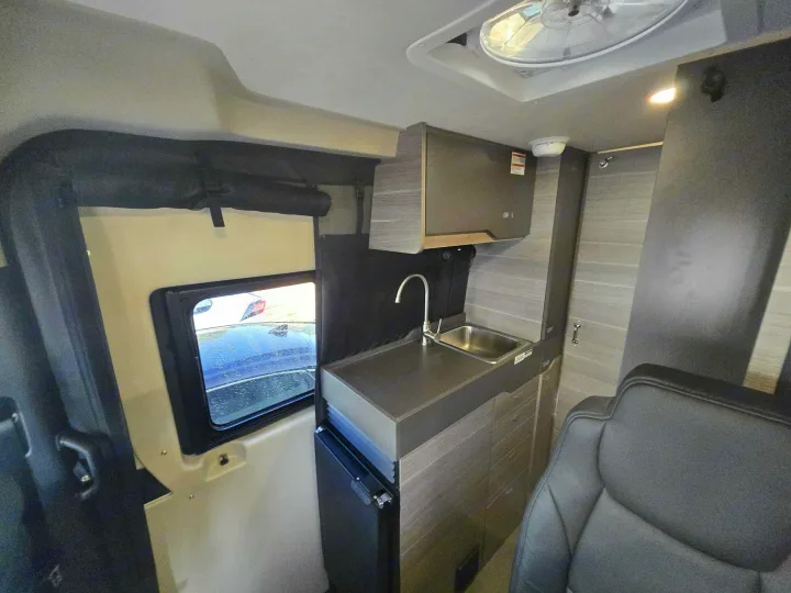 RV rental: Compact camper van interior with a kitchen counter, sink, overhead cabinet, small fridge, and front seat.. Entegra Launch Sprinter High Roof AWD 4x4 Camper Van 2025