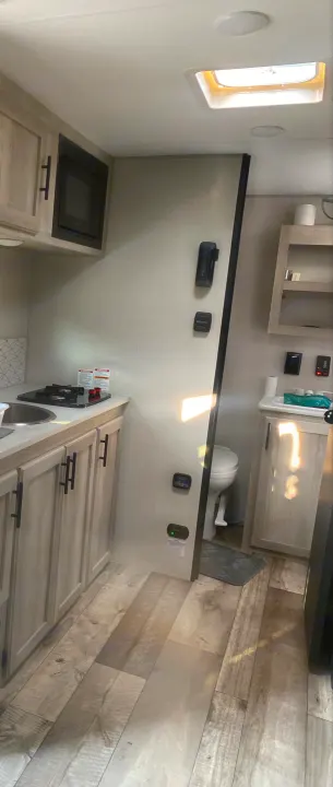 Inside a modern RV rental: well-equipped kitchen, compact bathroom, and warm sunlight illuminating the wood floors.. KZ Escape 2021