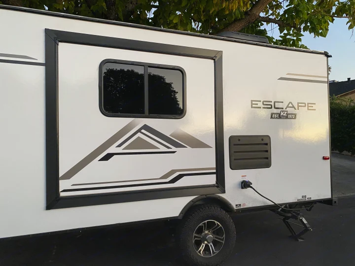 Side of a white K-Z Escape travel trailer with mountain graphics, power connected; perfect for an RV rental.. KZ Escape 2021