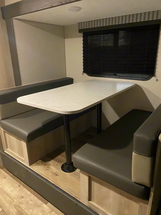 Enjoy meals in this comfortable RV rental dinette booth, featuring dark gray cushioned benches and a light tabletop in a modern camper.. KZ Escape 2021