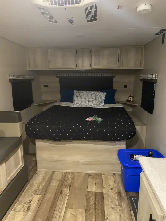 Inside an RV rental: a neat bedroom featuring a comfortable bed, built-in storage, and wood-style flooring.. KZ Escape 2021
