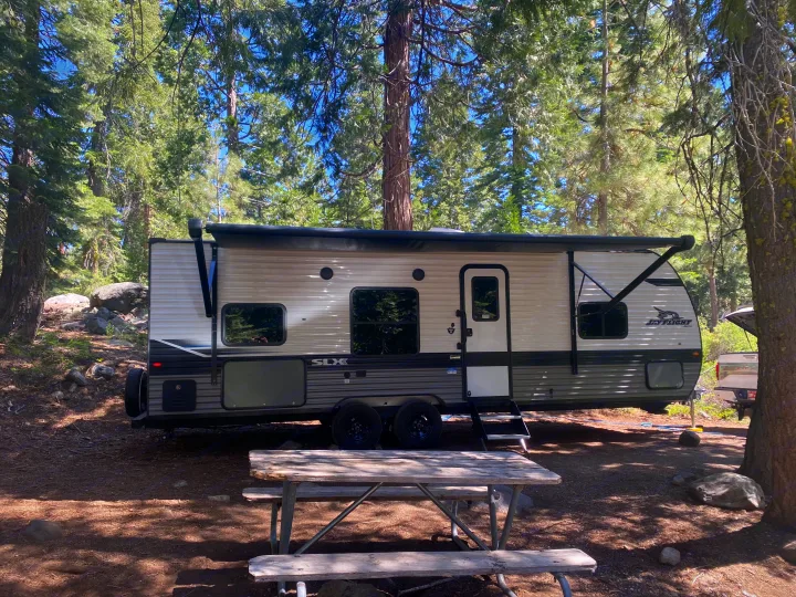 Spacious RV rental parked at a serene forest campsite with a picnic table, perfect for outdoor adventures.. Jayco Jay Flight SLX 2024
