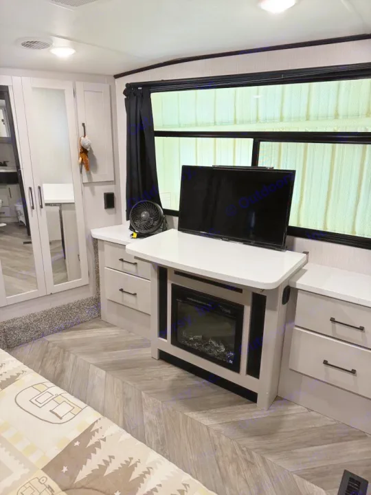 Modern RV rental interior showcasing a sleeping area, TV, electric fireplace, and light wood cabinetry for storage.. Heartland Cyclone 2022