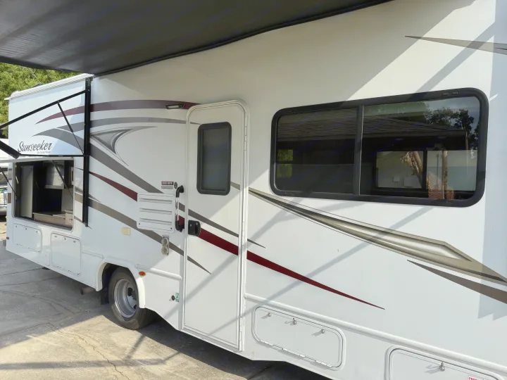 Side view of a white Sunseeker RV rental with an extended black awning and open outdoor kitchen.. Forest River Sunseeker 2017