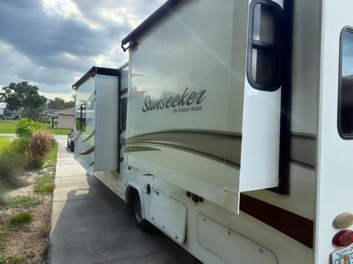 A white Sunseeker RV motorhome, with its slide-outs extended, parked on a driveway. Ideal for an RV rental adventure.. Forest River Sunseeker 2017