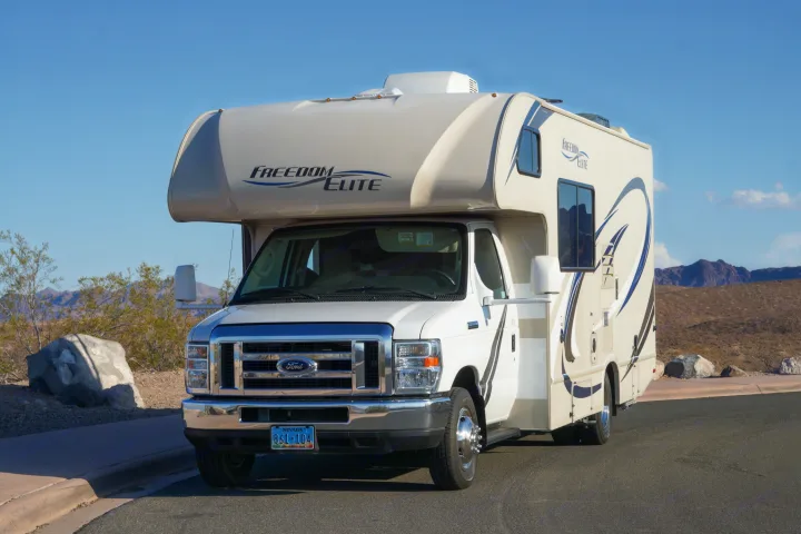 A white Class C Freedom Elite RV rental parked on asphalt in a desert landscape with mountains.. Thor Freedom Elite 2018