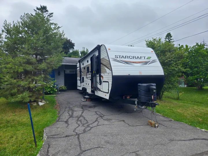 A white StarCraft travel trailer, an excellent RV rental option, parked on a paved driveway beside a house on a cloudy day.. Starcraft Autumn Ridge 2022