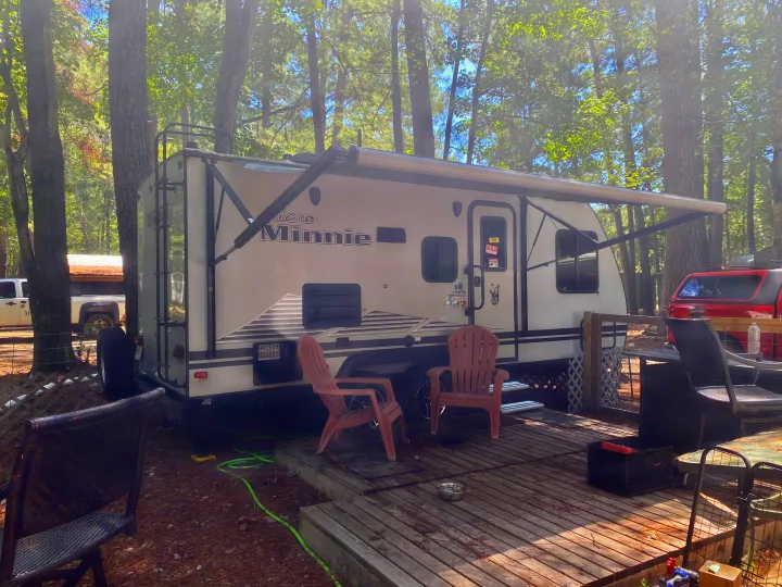 Cozy RV rental campsite: A Winnebago Micro Minnie travel trailer with awning extended, parked on a wooden deck with chairs.. Winnebago Minnie Winnie 2020
