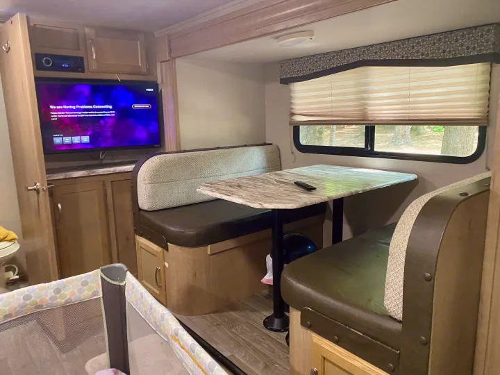 RV rental interior features a functional dinette, entertainment system, and a baby playpen, ideal for family trips.. Winnebago Minnie Winnie 2020