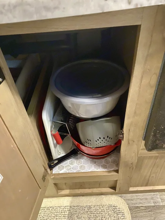 Inside an RV rental's kitchen cabinet: bowls, colander, and pans stacked for compact storage. Cooking essentials for your trip.. Winnebago Minnie Winnie 2020