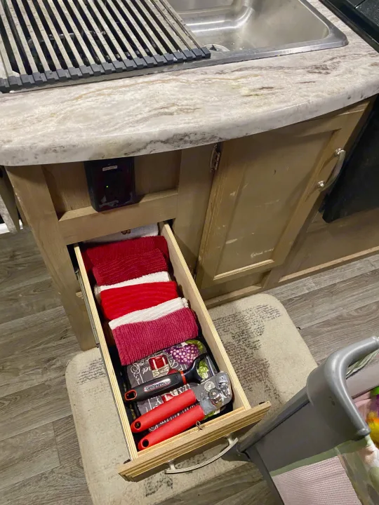 An rv rental kitchen: a drawer holds neatly folded dishtowels and kitchen utensils like a can opener, below a sink.. Winnebago Minnie Winnie 2020