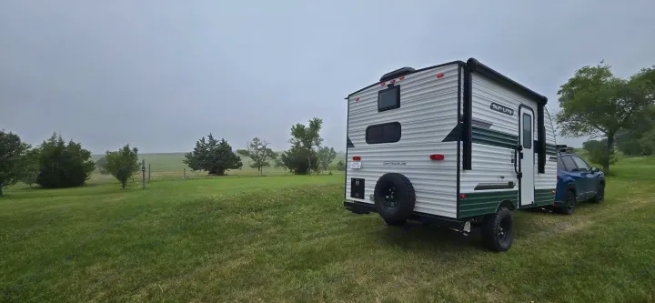 RV rental ready for adventure: A Sun Lite travel trailer and blue SUV parked in a vast green field under an overcast sky.. Sunset Park RV Sun Lite LTD 13MJ 2025