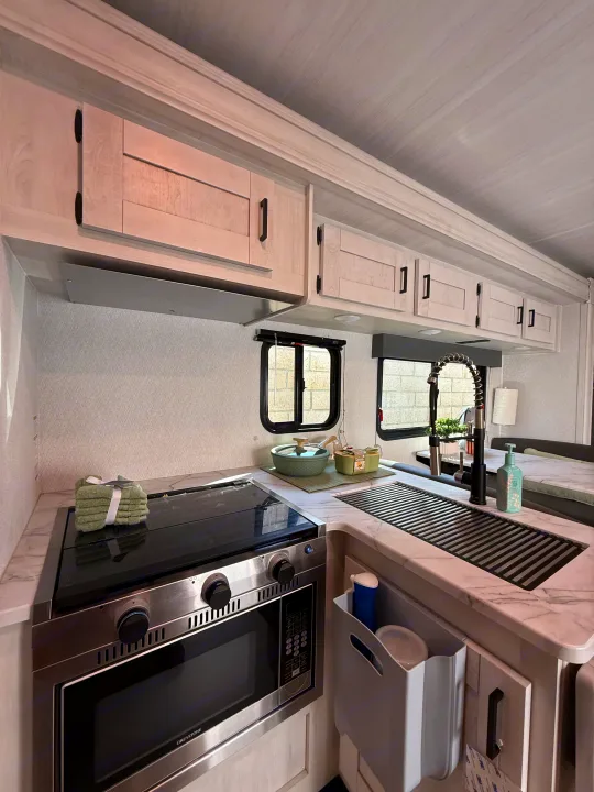 Inside a bright RV rental, this well-equipped kitchen has a stove, microwave, sink, and ample storage cabinets.. Forest River ENTRADA 3100FB 2024