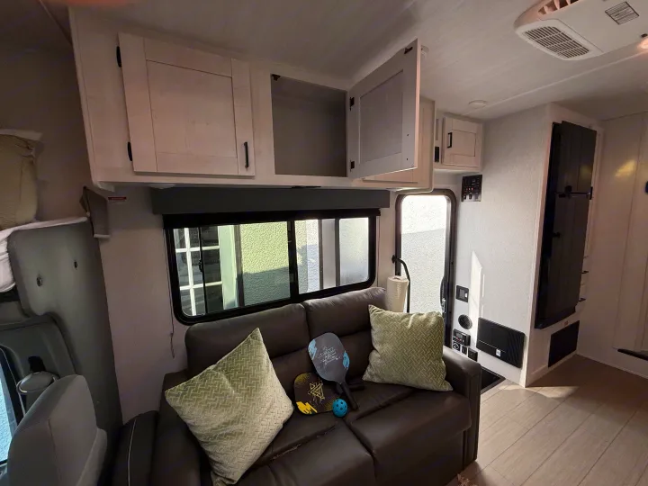 Inside this modern rv rental: a cozy living area with a dark sofa, bright pillows, ample storage in overhead cabinets, and large windows.. Forest River ENTRADA 3100FB 2024