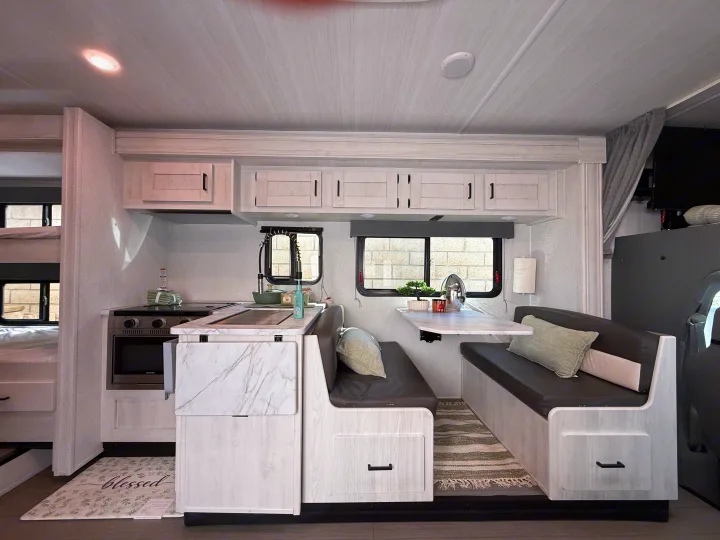 Modern RV rental interior with light wood cabinetry, a kitchen, dining area, and cozy bunk beds in the back.. Forest River ENTRADA 3100FB 2024