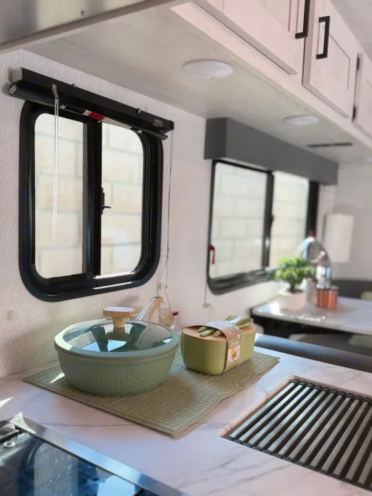Inside a modern RV rental: well-equipped kitchen with green cookware, sleek countertops, windows, and light cabinets.. Forest River ENTRADA 3100FB 2024