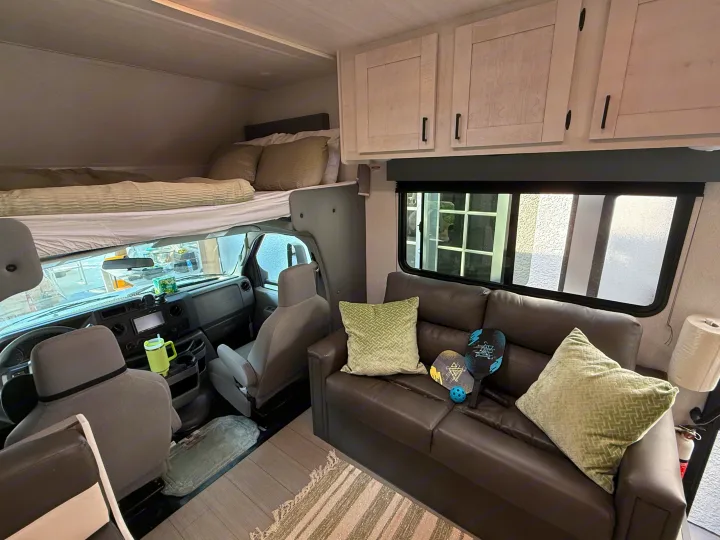 Cozy RV rental interior showing the front cab, overhead bunk bed, comfortable sofa, and storage cabinets. Perfect for your next adventure.. Forest River ENTRADA 3100FB 2024
