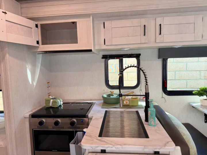 Functional RV rental kitchen with modern white cabinetry, a compact stove, and a versatile sink setup.. Forest River ENTRADA 3100FB 2024