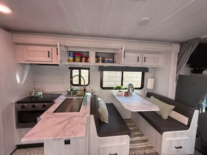 Inside an rv rental: a modern kitchen with a sink, stovetop, and stocked cabinets, plus a cozy dining booth with table.. Forest River ENTRADA 3100FB 2024