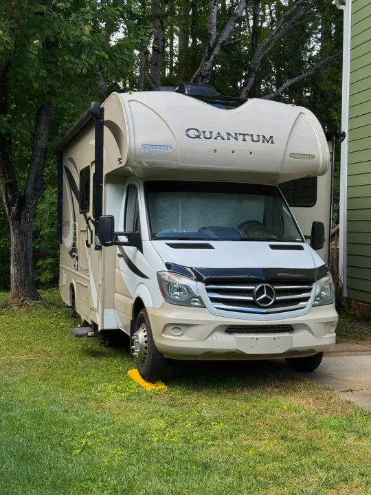A beige Mercedes-Benz Quantum Class C RV is parked on grass with leveling blocks, a common sight for an rv rental motorhome.. Thor Quantum 2018