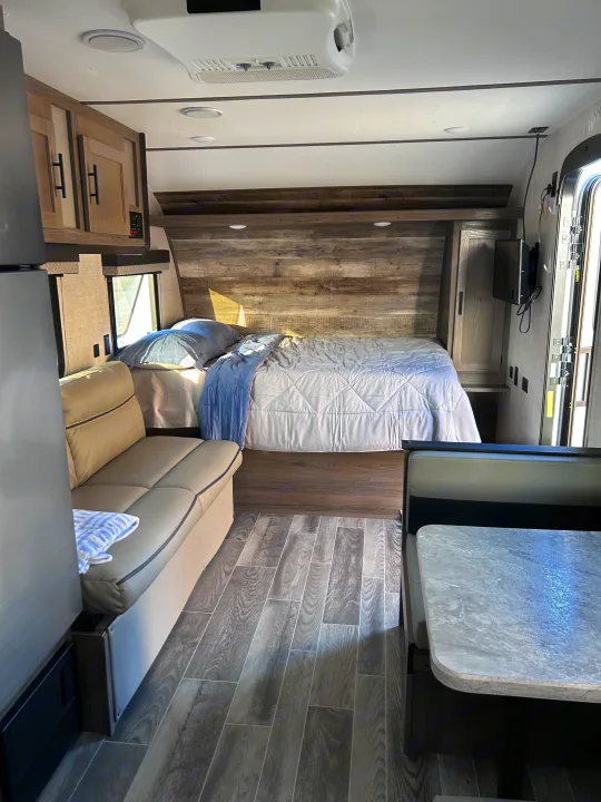 Spacious RV rental interior featuring a queen bed, sofa, and dining booth with wood-look flooring and modern cabinets.. Gulf Stream Ameri-Lite 2022