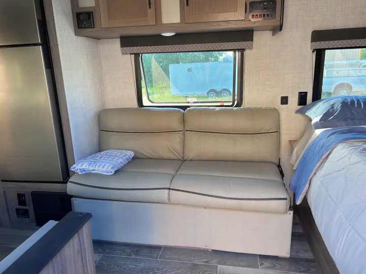 Spacious RV rental interior with a cozy sofa, large fridge, overhead cabinets, and a comfortable bed, ready for adventures.. Gulf Stream Ameri-Lite 2022