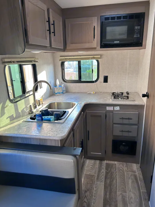Spacious RV rental kitchen showcasing a sink, microwave, two-burner cooktop, and light wood cabinetry, ideal for on-the-road living.. Gulf Stream Ameri-Lite 2022