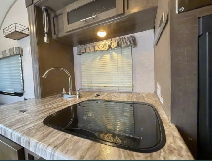 Compact RV rental kitchen features a modern sink, covered stovetop, and overhead cabinets.. R-Pod R-Pod Trailer 2018