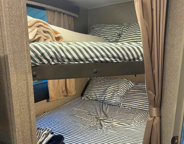 Cozy bunk beds in an RV rental, featuring striped bedding and privacy curtains, perfect for family adventures.. Forest River Rockwood Mini Lite 2020