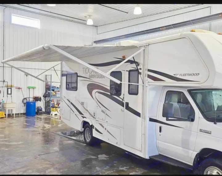 A white Fleetwood Tioga Class C rv rental with its awning extended, parked in a service bay, likely cleaned.. Tioga Montara 2012