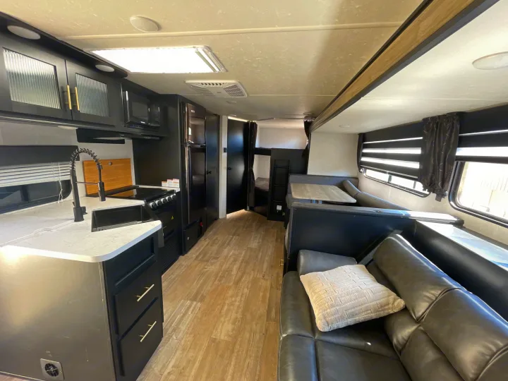 Explore this modern RV rental interior featuring a kitchen, dining booth, and cozy bunk beds. Ideal for travel & camping.. Forest River Cherokee Grey Wolf 2021