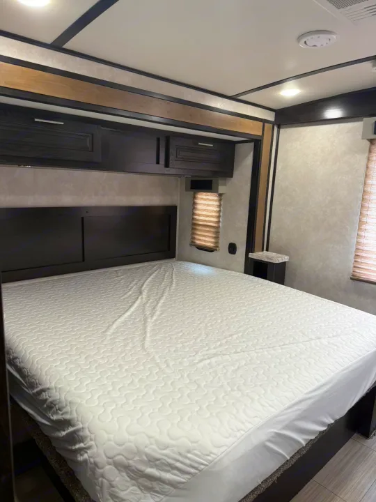 Spacious, clean RV rental bedroom with a large, inviting bed, dark wood headboard, and convenient overhead cabinets.. Forest River FR3 2019