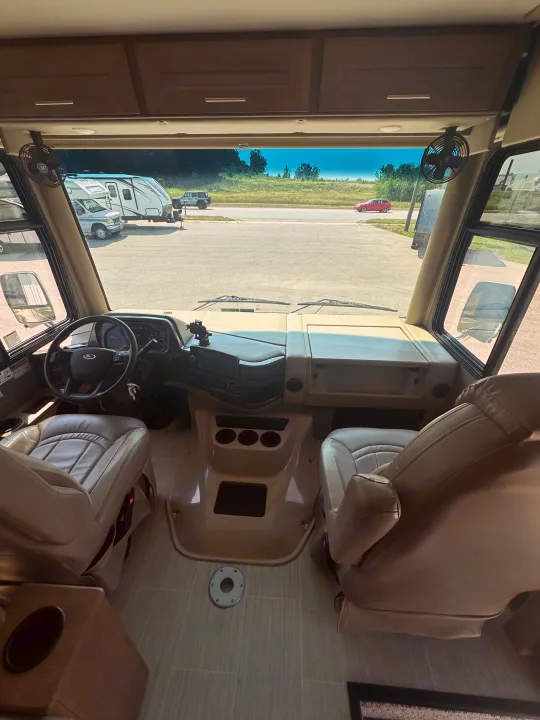 Experience RV rental comfort: interior front view of an RV, featuring seats, dashboard, and a road view through the windshield.. Thor Challenger 2022
