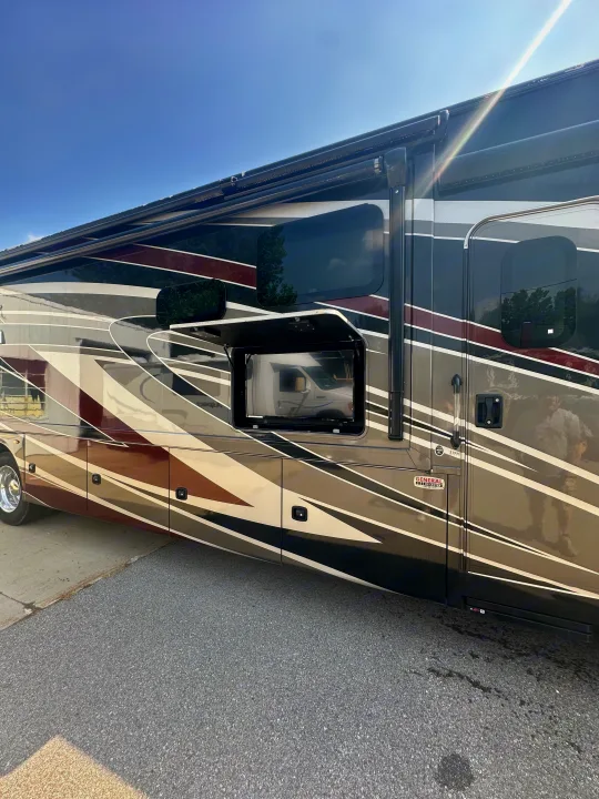 Luxury RV rental side view: a modern motorhome with bold stripes and an open compartment revealing an outdoor TV.. Thor Challenger 2022