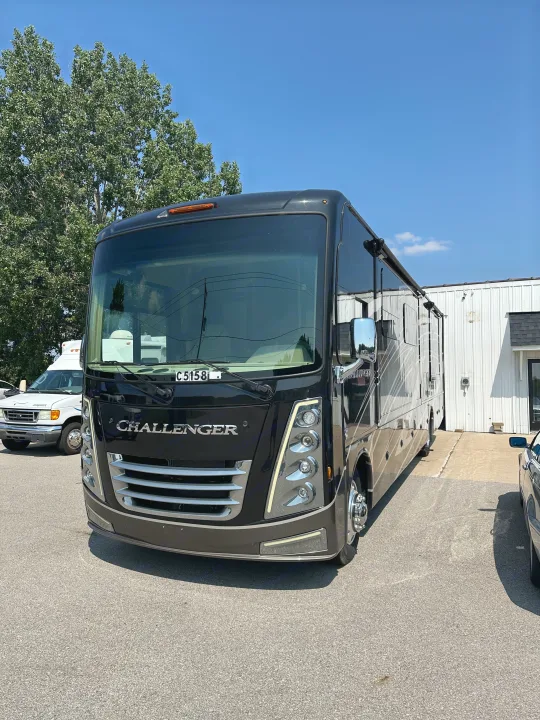Sleek black Challenger Class A RV available for rental. Parked in a lot under a clear blue sky, next to a white van.. Thor Challenger 2022