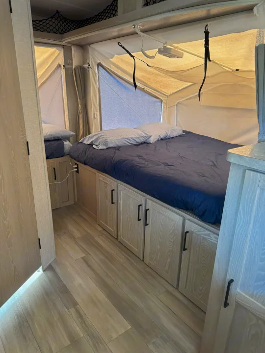This inviting RV rental bedroom features a comfy bed with blue bedding, under-bed storage cabinets, and pop-out tent walls.. Rockwood Roo 2022