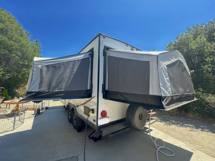 This RV rental, a white hybrid travel trailer, features extended pop-out tent beds ready for outdoor camping.. Rockwood Roo 2022